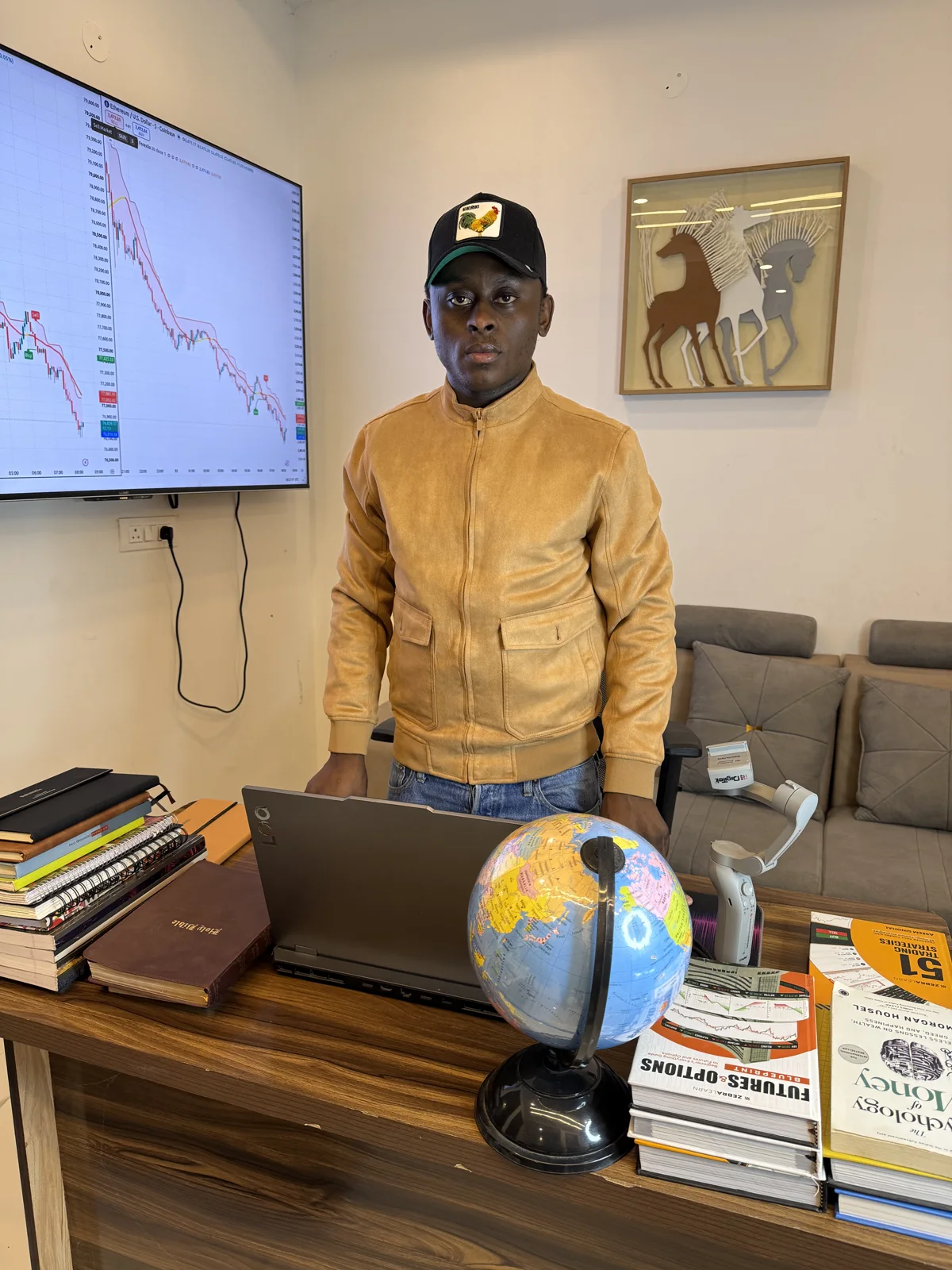 An AfriGlobal representative standing at a Trading Avenue desk with a laptop, a globe and a stack of trading books