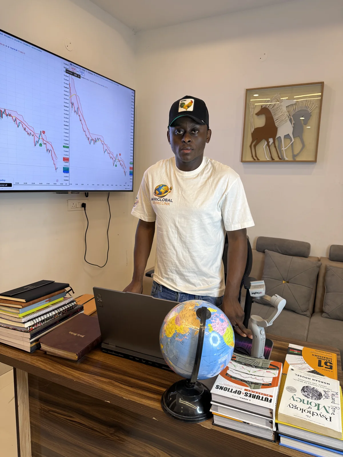 An AfriGlobal representative at a Trading Avenue workstation, with a market chart on the wall screen and trading books on the desk